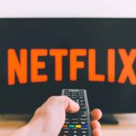 viewer holding a remote control pointed towards a television screen displaying the Netflix logo
