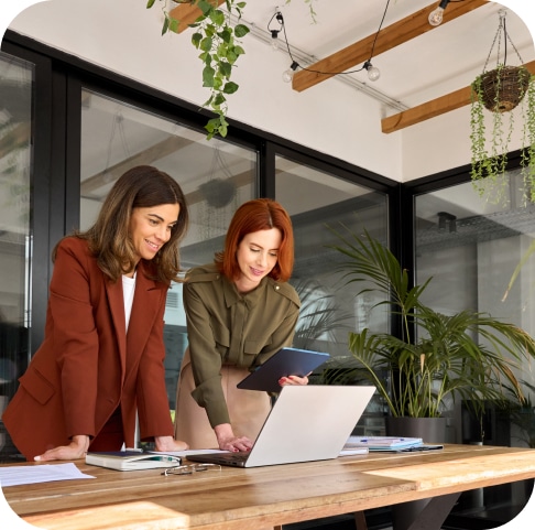 Two professional women smiling while reviewing laptop together in modern office